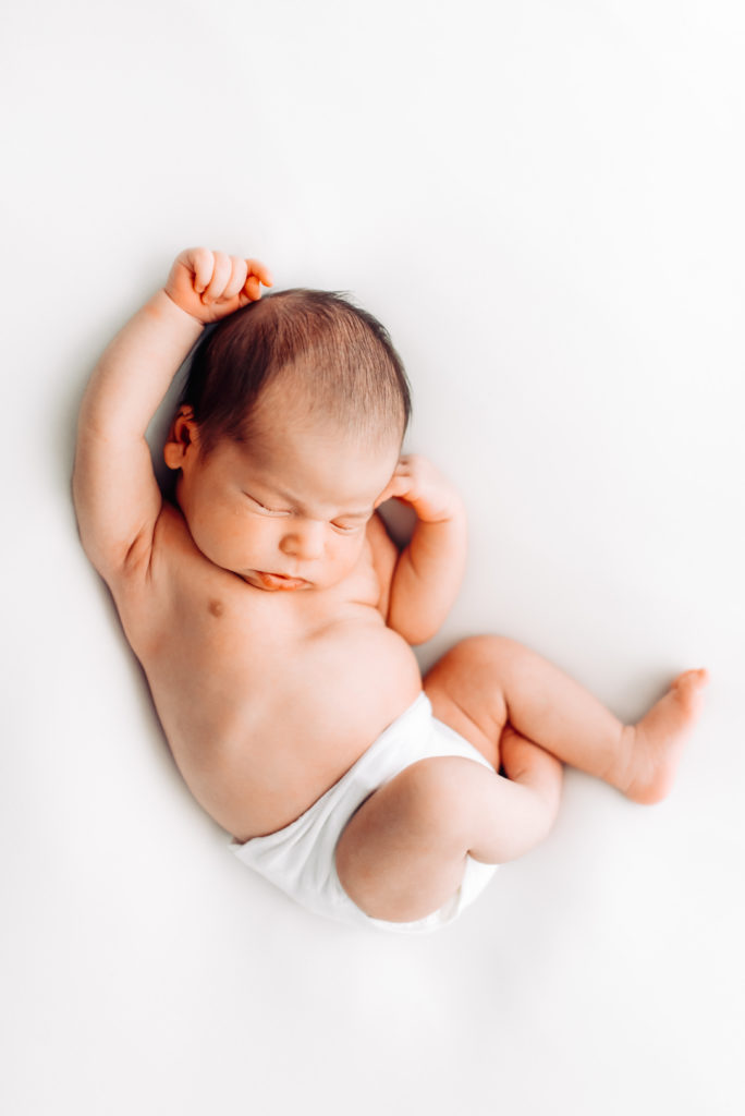 Newborn photography, a baby lays on a white sheet sleeping