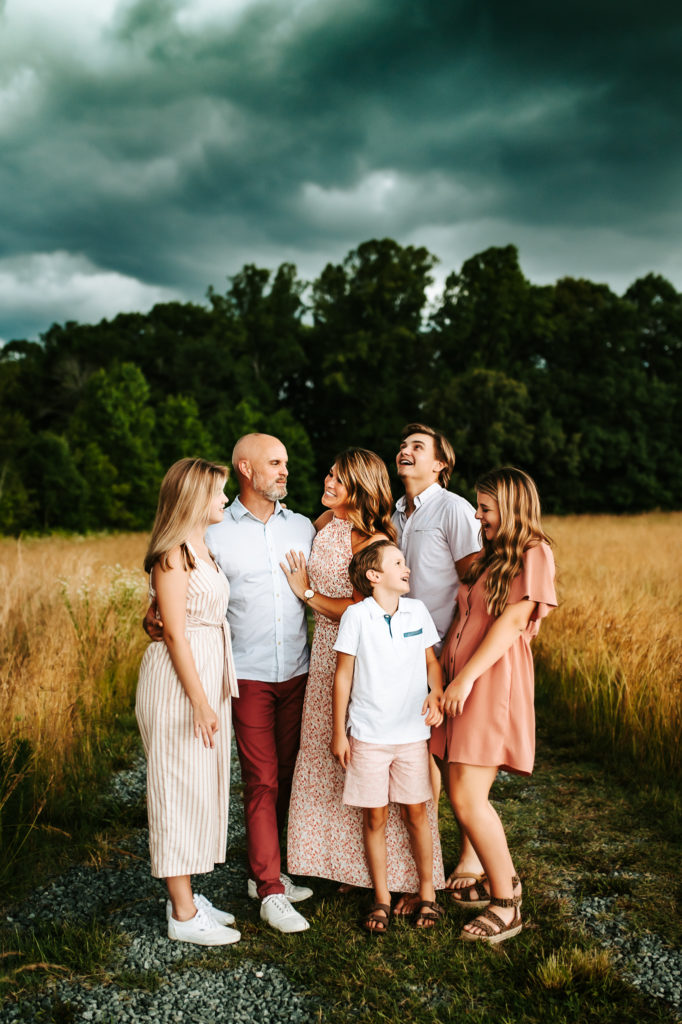 Family Photographer, mom and dad stand with their four children in a meadow
