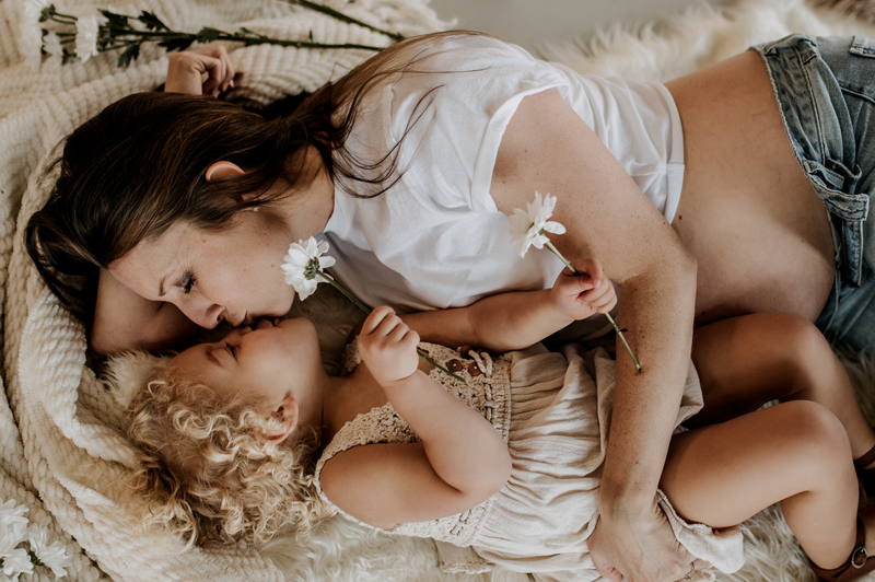Family Photographer, a mother kisses her young daughter as they snuggle in blankets